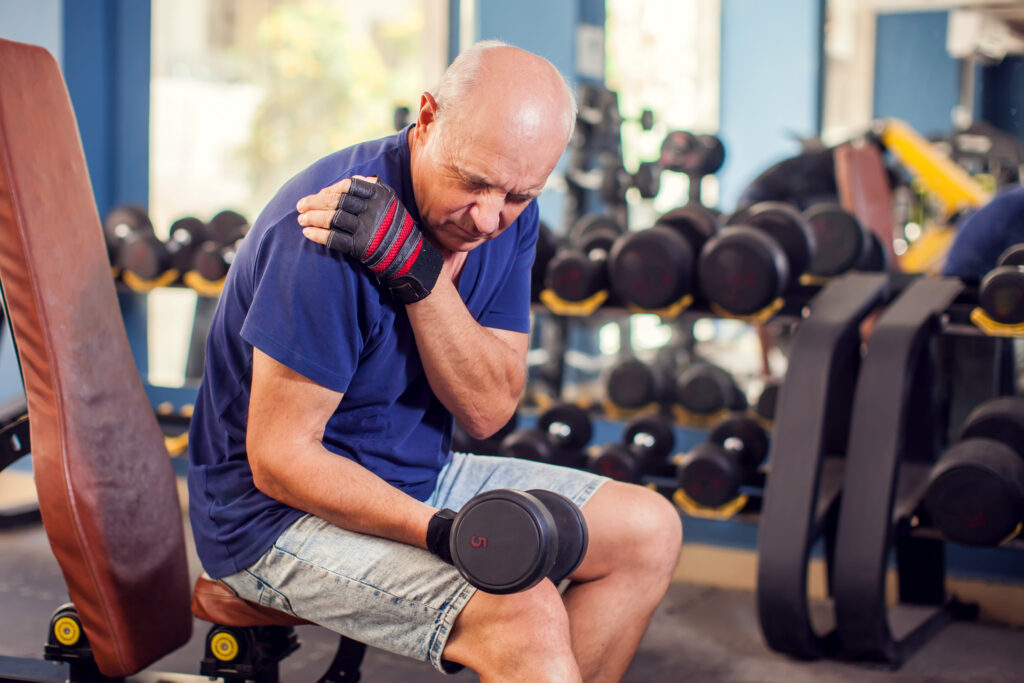 Senior Man Feeling Strong Shoulder Pain at the gym from lifting weights after his shoulder replacement.